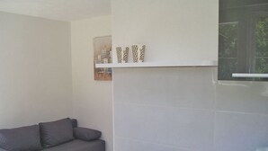 Un salon moderne avec un canapé gris, un mur blanc et une petite étagère ornée d’objets décoratifs.