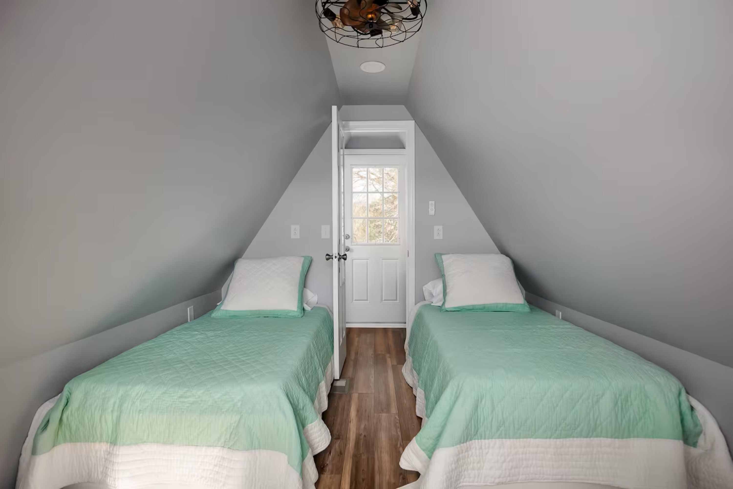 Une chambre avec deux lits, une porte blanche et un plafond en pente.