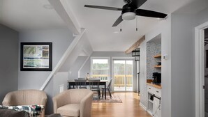 A spacious living room with a high ceiling, a ceiling fan, a dining area with a table and chairs, and a kitchen area with wooden cabinets and a countertop. - MountainWaters - Mtn, River, Relax! - Hottub, Private Riverfront, Firepit. (Maurertown)