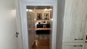 A hallway with a wooden floor leading to a dark-colored sofa and a white cabinet. - Suite 49 (Brasov)