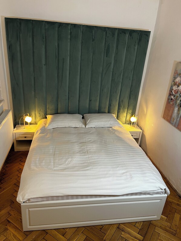 A bedroom with a large bed, two bedside tables with lamps, a radiator, and a wooden floor. - Suite 49 (Brasov)