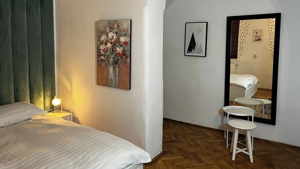 A bedroom with a bed, a nightstand, a lamp, a mirror, and two framed pictures on the wall. - Suite 49 (Brasov)