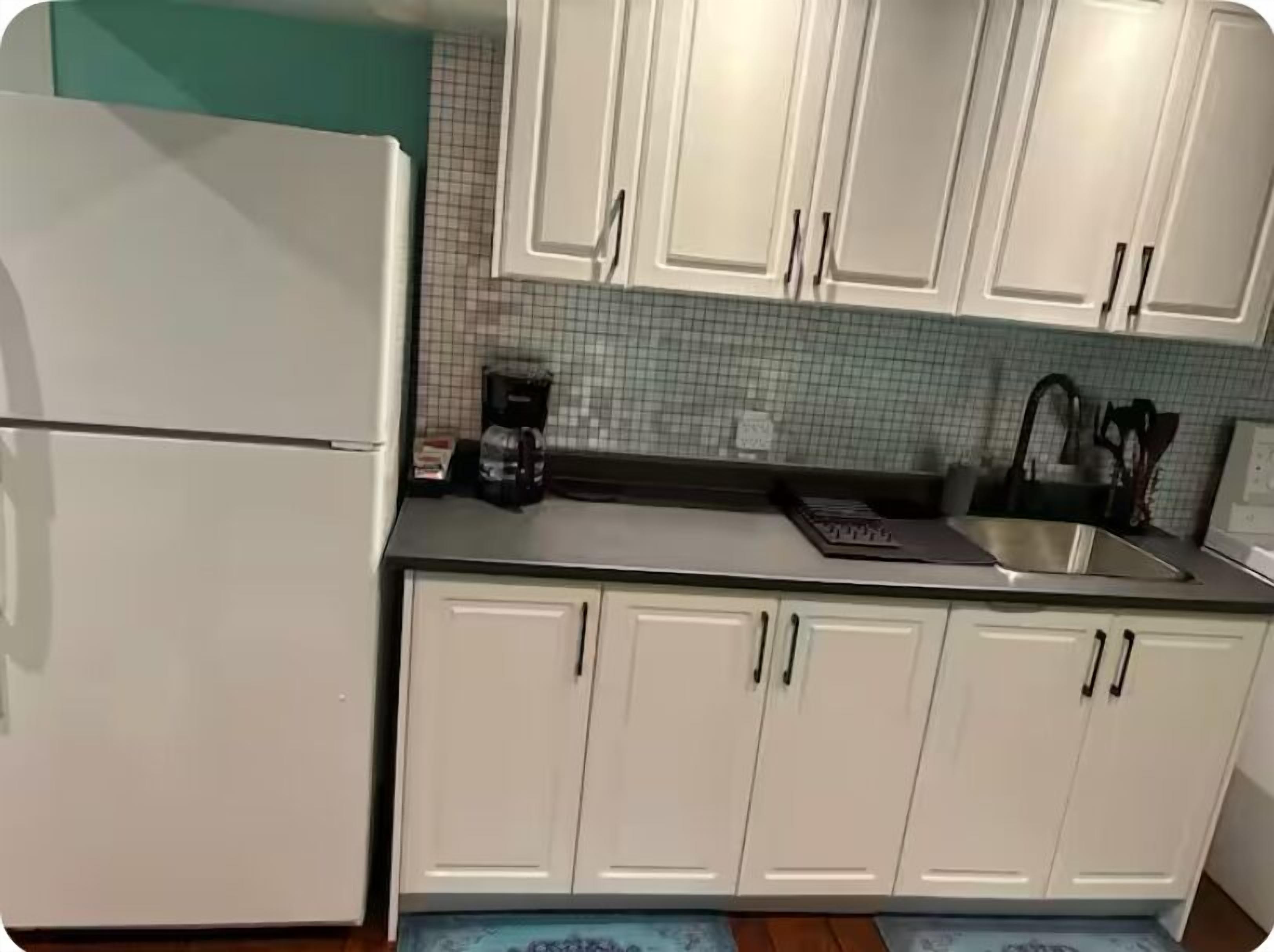 A kitchen with white cabinets, a refrigerator, a coffee maker, and a sink.