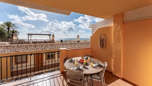 A balcony with a tiled floor, a round table set for dining, and a view of the sea and buildings in the distance.