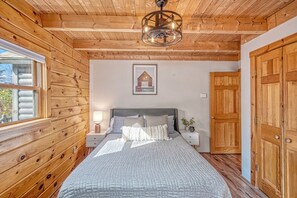 Une chambre à coucher aux murs lambrissés, avec un lit, des tables de chevet, une petite table, un tableau encadré au mur et une porte en bois.