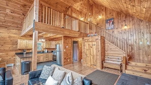 Une cabane en bois spacieuse avec une chambre à coucher en mezzanine, une cuisine et un espace de vie comprenant un canapé et une cheminée.