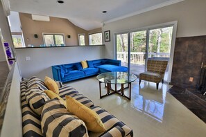 Una sala de estar con un sofá azul, uno a rayas y un sillón estampado, una mesa de centro de vidrio y una chimenea.