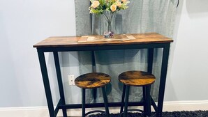 Un tavolo di legno con due sgabelli, un vaso con fiori e una tenda grigia sullo sfondo.
