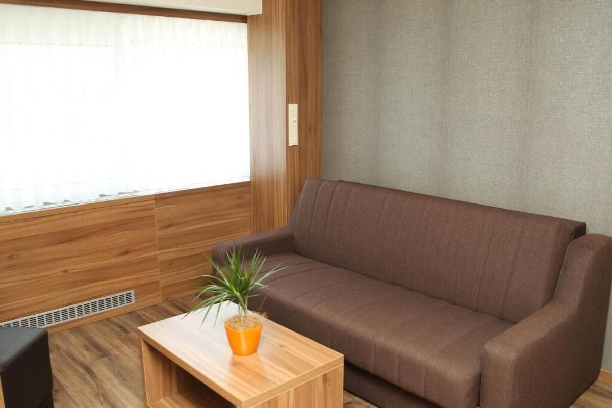 A room with a brown sofa, a wooden coffee table with a potted plant, and a window with blinds.