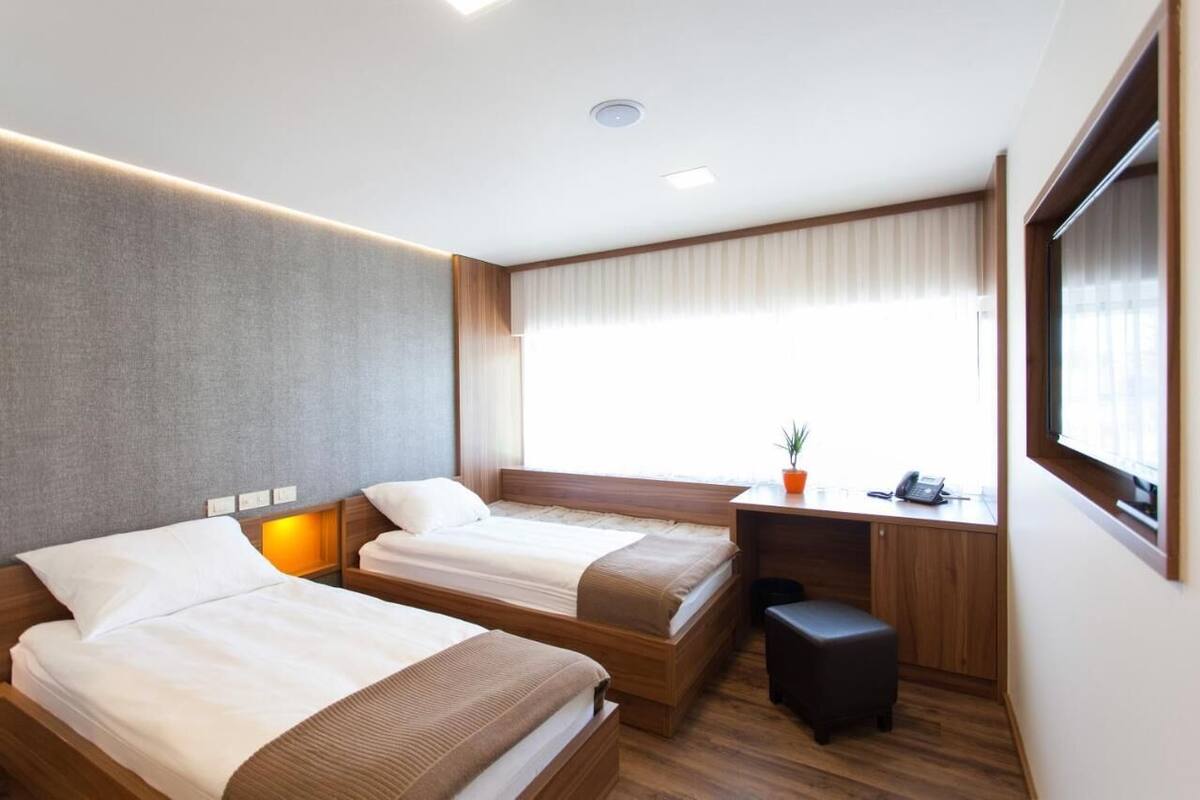 A hotel room with two beds, a desk, a chair, a small table, and a window with curtains.