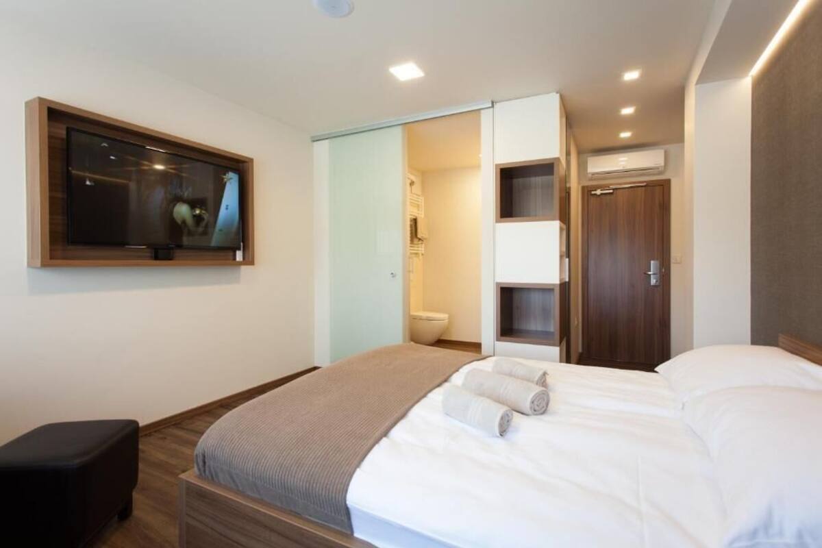 A modern hotel room with a bed, a TV, a wardrobe, and a bathroom.