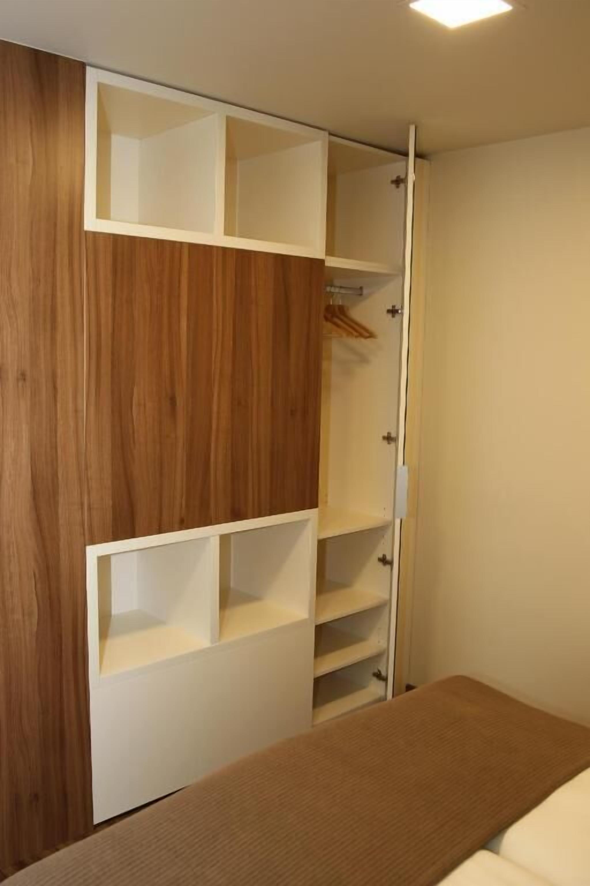 A bedroom with a wooden wardrobe, a bed, and a bedside table.