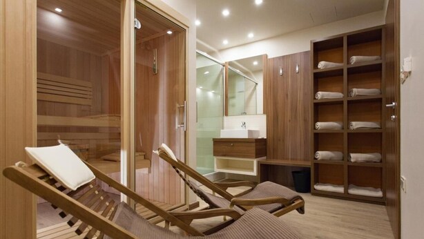 A sauna room with wooden benches, a glass door, and a wooden cabinet with towels. - Hotel Pomaranča (Ptuj)