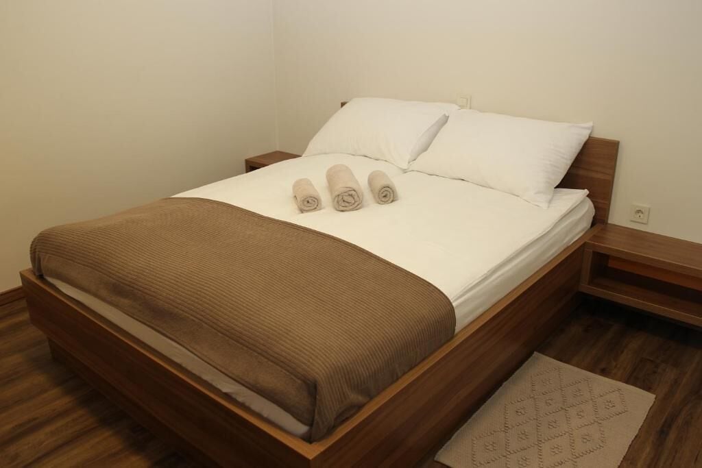 A neatly made bed with a brown headboard, white linens, and three rolled towels.