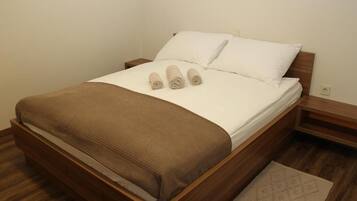 A neatly made bed with a brown headboard, white linens, and three rolled towels.