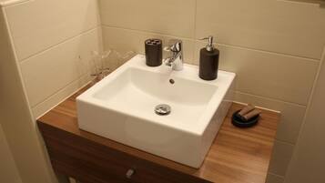 Un baño con lavamanos blanco, encimera de madera y un espejo encima.