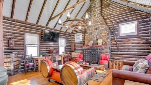 A log cabin interior with wooden floors, a stone wall, a fireplace, and a television mounted on the wall.