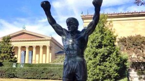 Una estàtua d'un boxejador a un parc amb un edifici clàssic al fons.