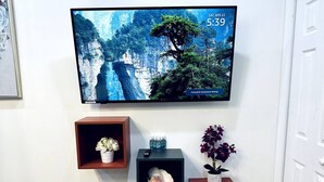 Een aan de muur bevestigde televisie toont een sfeervol natuurbeeld met datum en tijd. Daaronder bevinden zich drie houten planken met diverse decoratieve objecten.