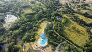 Vista aérea de un complejo turístico con piscina rodeada de exuberante vegetación y senderos sinuosos.