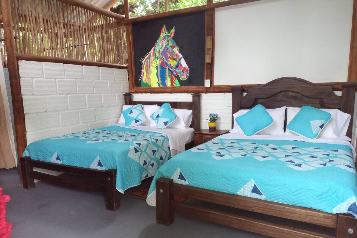 Een kamer met twee houten bedden, elk met een blauwe sprei en bijpassende kussens. Aan de muur boven de bedden hangt een kleurrijk schilderij van een paard.