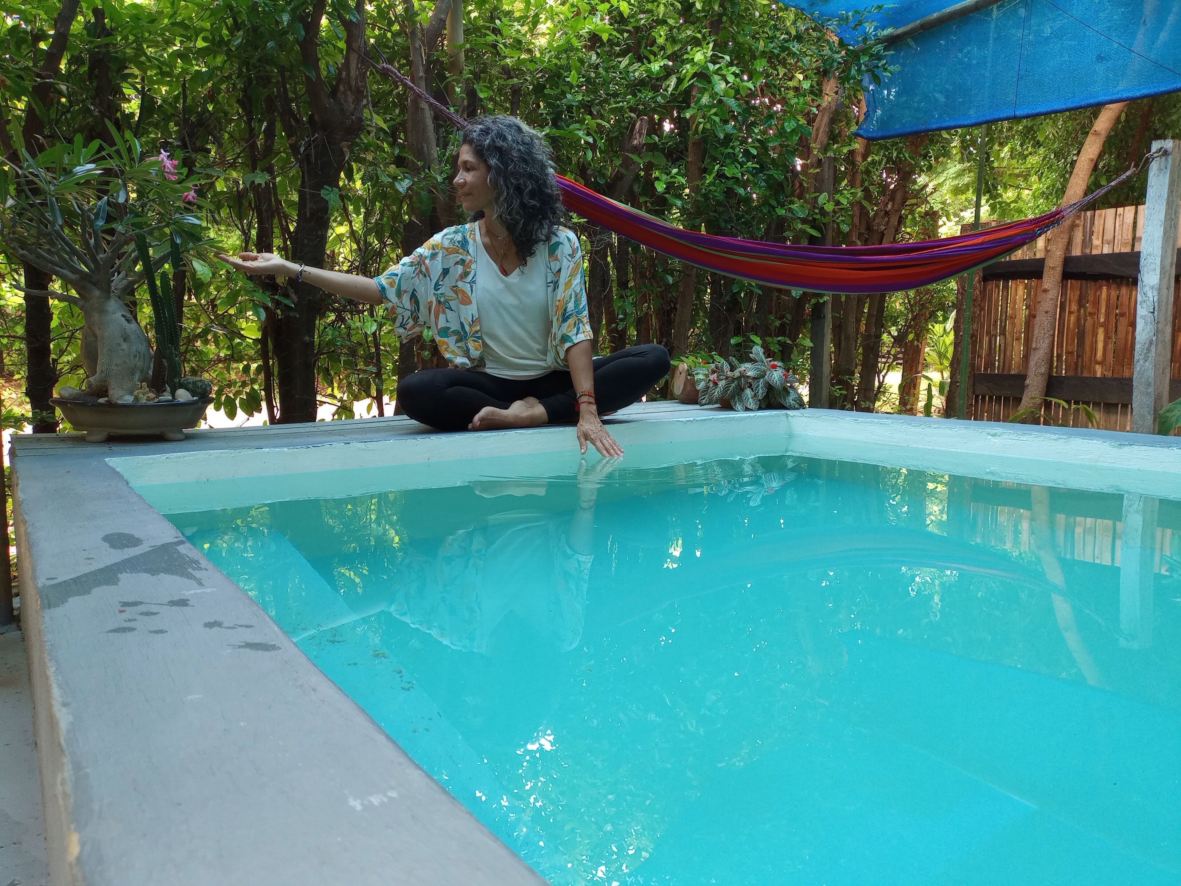 A person sitting by a small pool with a hammock and plants around.