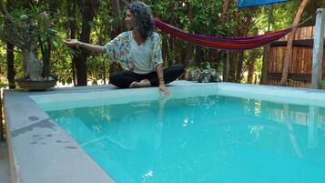 A person sitting by a small pool with a hammock and plants around.