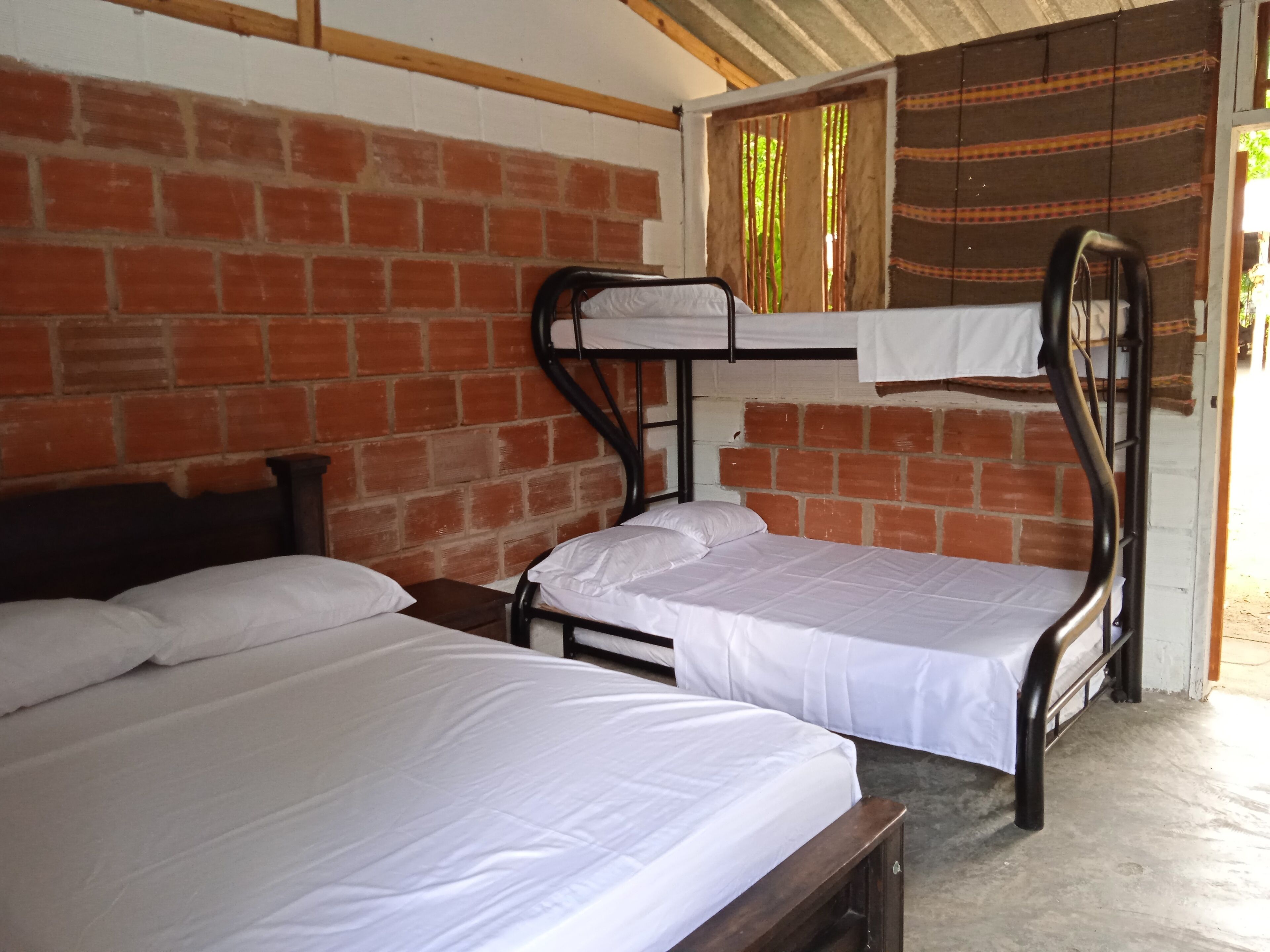 Una habitación con dos literas, una pared de ladrillo y un ventanal con cortinas.