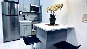 A modern kitchen with stainless steel appliances, a built-in microwave, grey cabinets, and a white island with bar stools. - New! Suite by Rittenhouse Square! (Philadelphia)