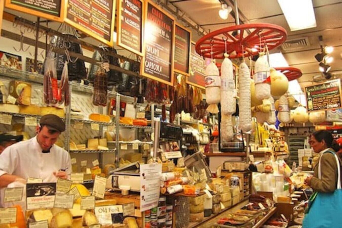 A cheese shop with shelves of various cheeses and hanging cheese wheels.