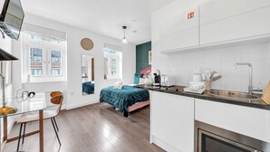 A modern kitchen with a sink, stove, and a dining area with a glass table and chairs. - City Life in Style: Chic Studio in Prime Area (London)