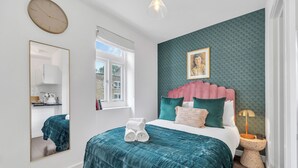 A bedroom with a teal bedspread, a large mirror, a clock, and a green textured wall. - City Life in Style: Chic Studio in Prime Area (London)