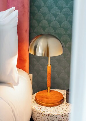A bed with white bedding, a round wooden nightstand with a speckled tablecloth, and a modern lamp with a wooden base and metallic shade. - City Life in Style: Chic Studio in Prime Area (London)