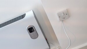 A white air conditioning unit with a remote control and a power cord plugged into a wall socket. - City Life in Style: Chic Studio in Prime Area (London)