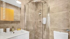 A modern bathroom with a glass-enclosed shower, a white sink with a gold faucet, and a beige tiled wall. - City Life in Style: Chic Studio in Prime Area (London)