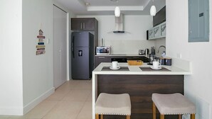 A modern kitchen with a refrigerator, microwave, and coffee maker. There are two stools and a small table with cups. - Airy modern apartment king bed w/pool (Kingston)