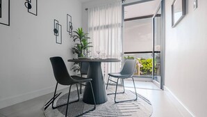 A modern dining area with a round table, two chairs, a potted plant, and a view of a balcony. - Airy modern apartment king bed w/pool (Kingston)