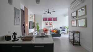 A modern kitchen with a central island, a dining area with a sofa and chairs, a TV, and a ceiling fan. - Airy modern apartment king bed w/pool (Kingston)