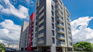 A multi-story building with a modern architectural design, featuring a prominent red vertical element on the left side. - Airy modern apartment king bed w/pool (Kingston)