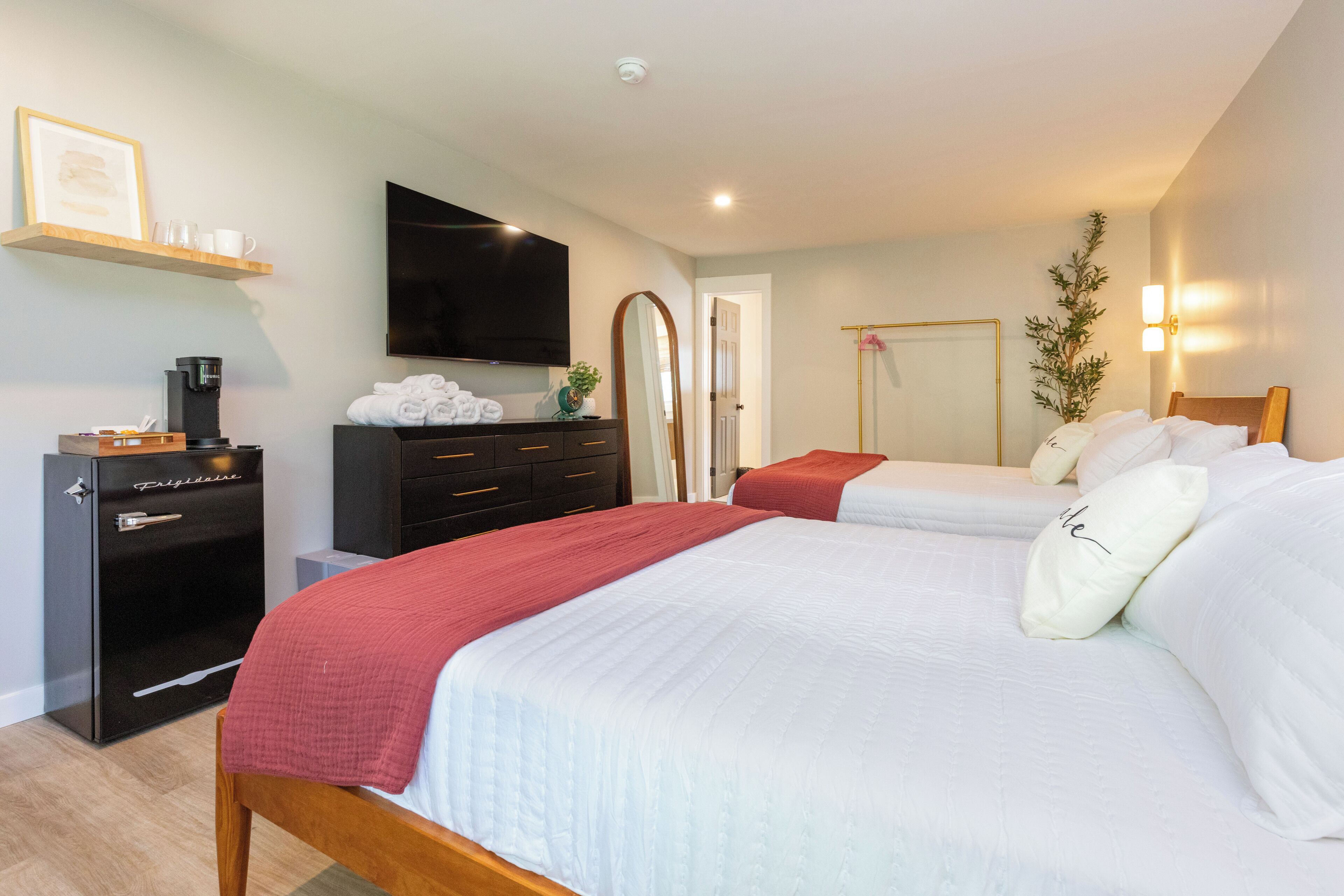 A hotel room with two beds, a TV, a coffee machine, a wardrobe, and a mirror.