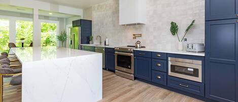 A modern kitchen with marble countertops, stainless steel appliances, and dark blue cabinetry.