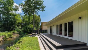 Et moderne hus med terrasse, en lille udendørs siddeplads og en flod i nærheden.