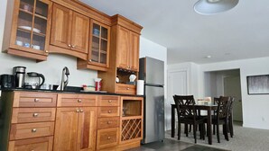 A kitchen with wooden cabinets, a stainless steel refrigerator, and a dining area with wooden chairs. - Charming 2-bedroom guest suite in the prime location of Fredericton (Fredericton)