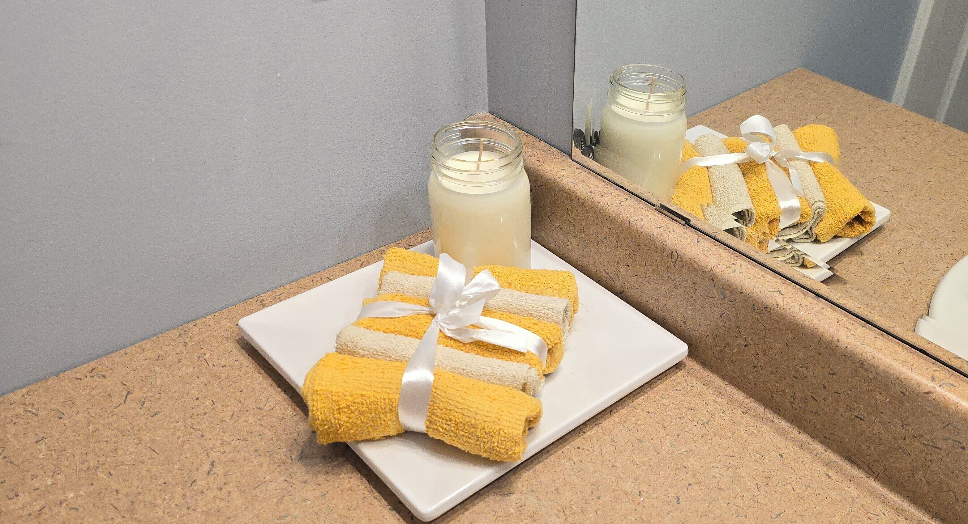 A bathroom with a white sink, a mirror, and a plate with yellow towels tied with a white ribbon.