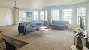 A spacious living room with a grey sectional sofa, a white coffee table, and a grey armchair. There is a large window providing natural light and a view of the outdoors. - Charming 2-bedroom guest suite in the prime location of Fredericton (Fredericton)