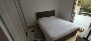 A small, modern bedroom with a single bed, a dark headboard, and a patterned rug. - LE WISSEL Charming T3, 2 bedrooms and 3 beds, very quiet 3 minutes from the center of Neuville (Neuville-sur-Saône)