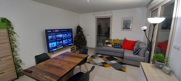 A living room with a TV, sofa, and a Christmas tree. - LE WISSEL Charming T3, 2 bedrooms and 3 beds, very quiet 3 minutes from the center of Neuville (Neuville-sur-Saône)
