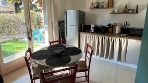 Una cucina con frigorifero, forno a microonde e macchina del caffè. È presente un tavolo da pranzo con sedie e vista su un giardino tramite una porta scorrevole in vetro.