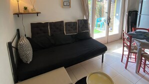 Un soggiorno con un divano nero, un tavolino, una lampada e una porta scorrevole in vetro che dà su una zona esterna.