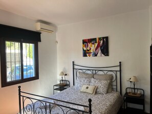 Un dormitorio con una cama, dos mesitas de noche, un ventanal y un equipo de aire acondicionado.